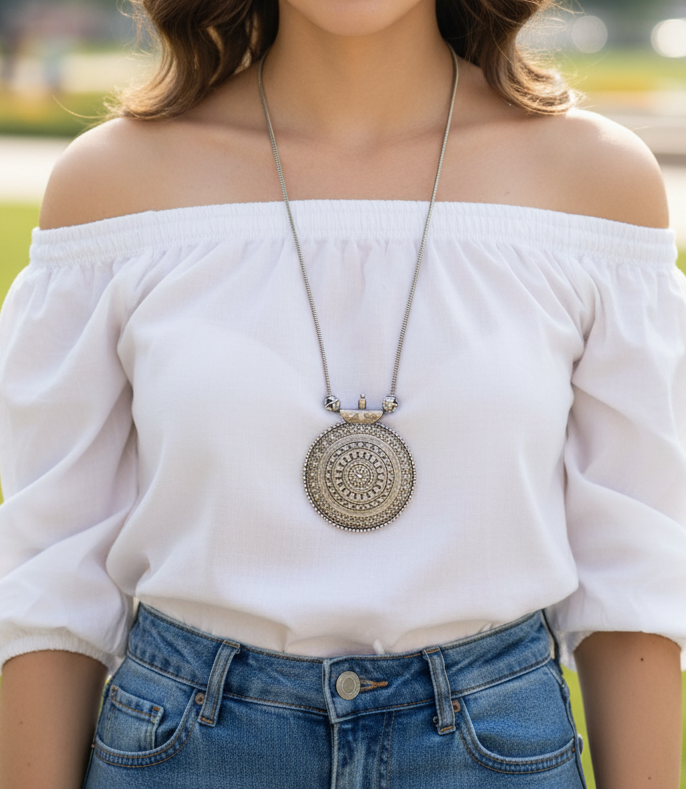 Silver pendant necklace featured on a woman in a white off-shoulder top, with intricate detailing.