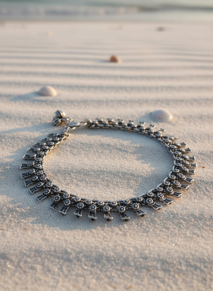 Elegant silver bracelet with floral details, resting on sandy beach background.