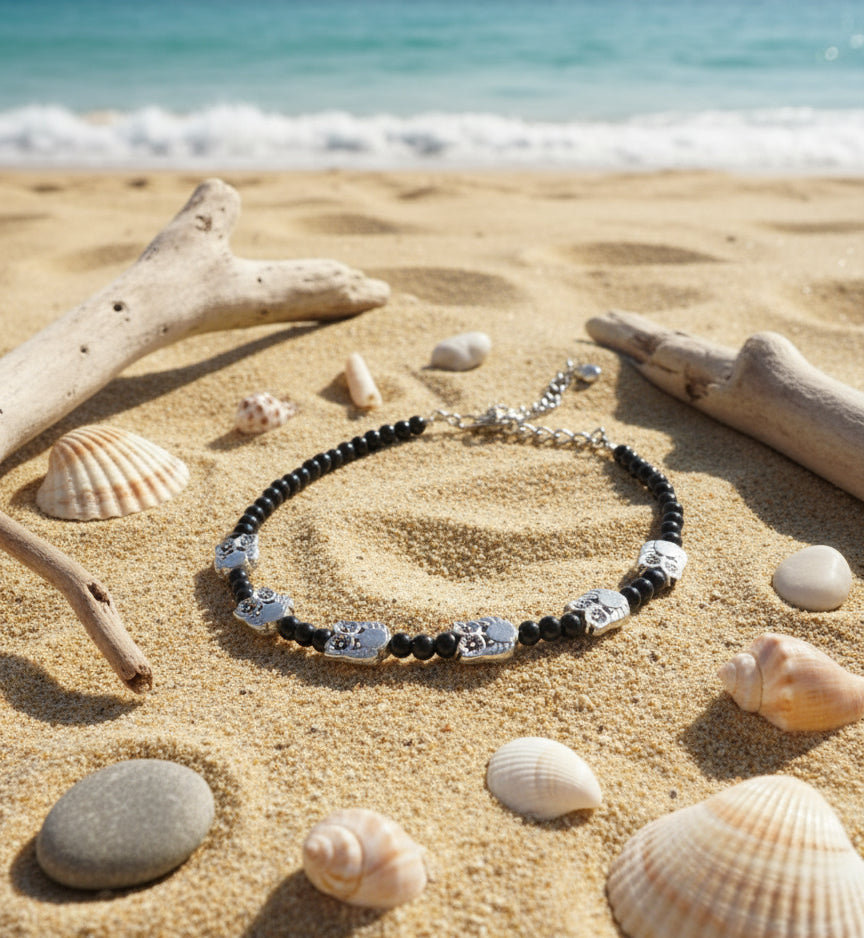 Black bead necklace with silver skull charms, perfect beach accessory on sandy shore.