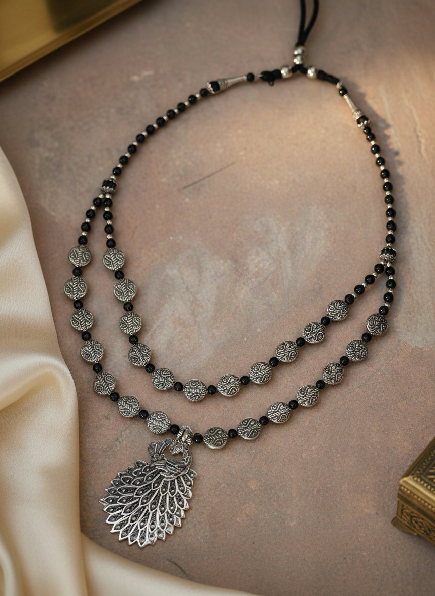 Elegant black beaded necklace with silver peacock pendant and intricate metallic details.