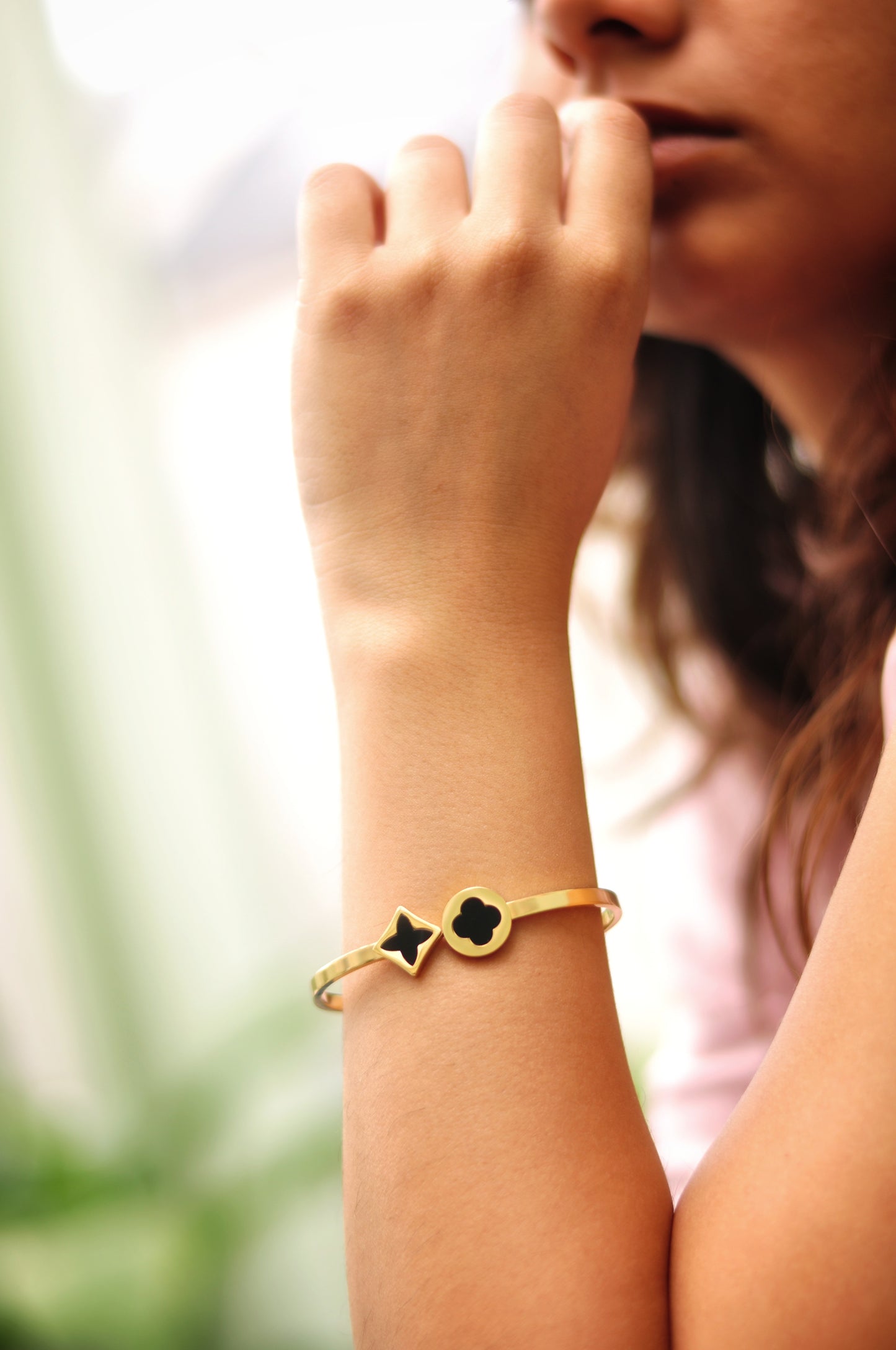 Gold bangle bracelet with black star and clover charms, perfect for stylish accessorizing.