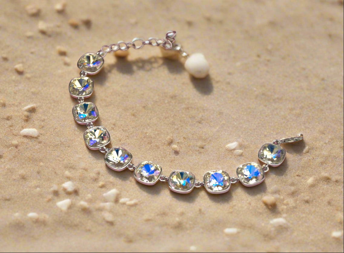Elegant silver bracelet with sparkling colorful crystals on a sandy background.