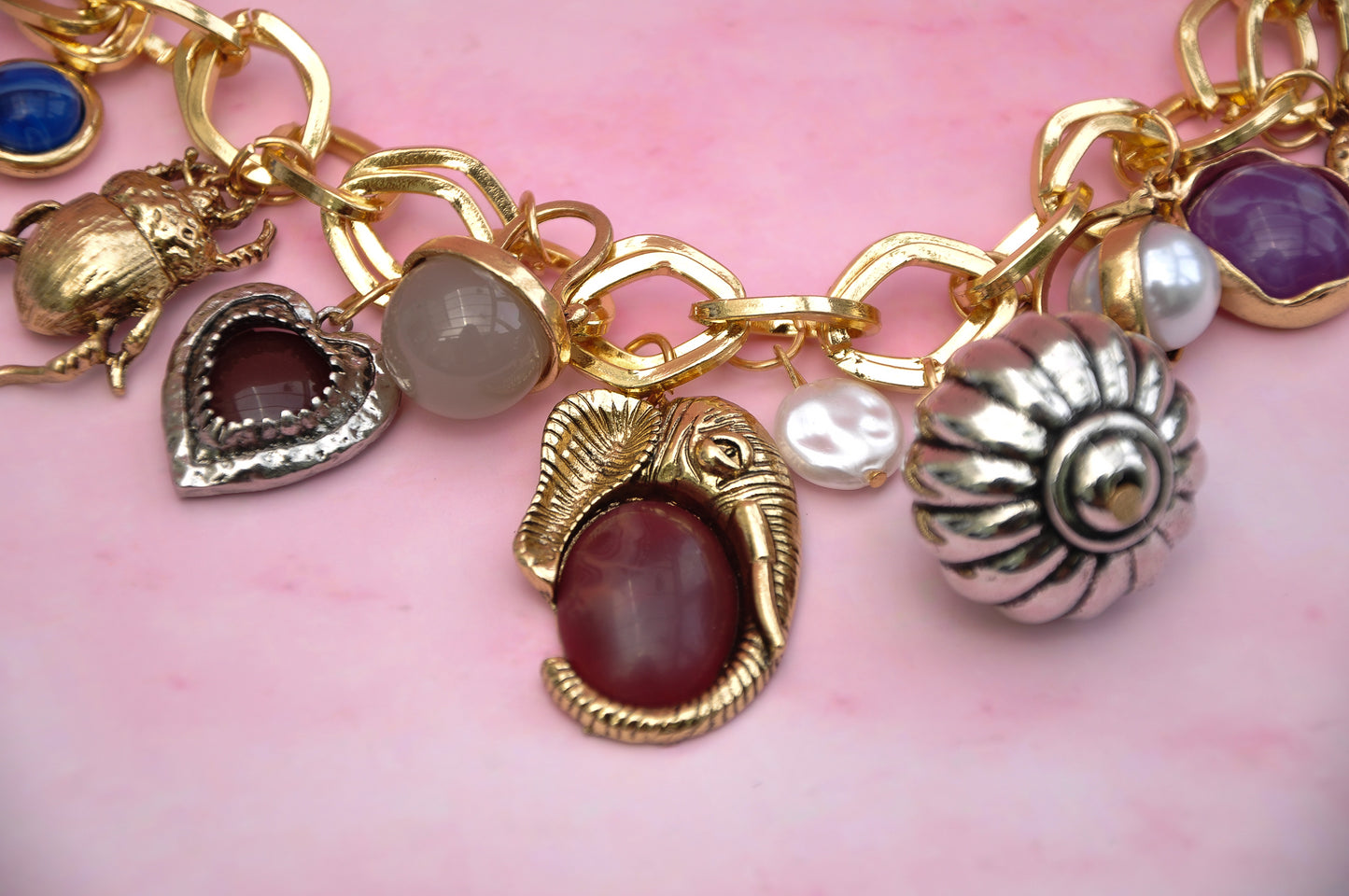 Gold charm bracelet with elephant, heart, and colorful gemstones on a pink background.