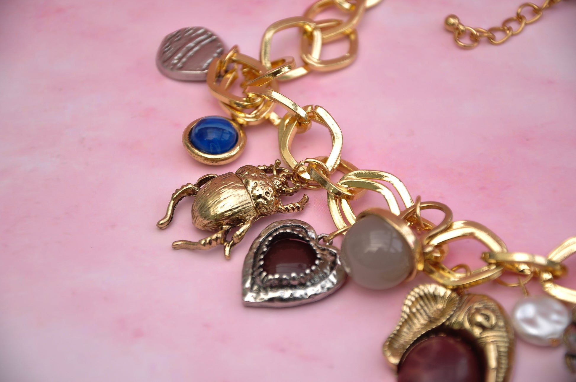 Gold charm bracelet with assorted charms including scarab, heart, and colored stones.