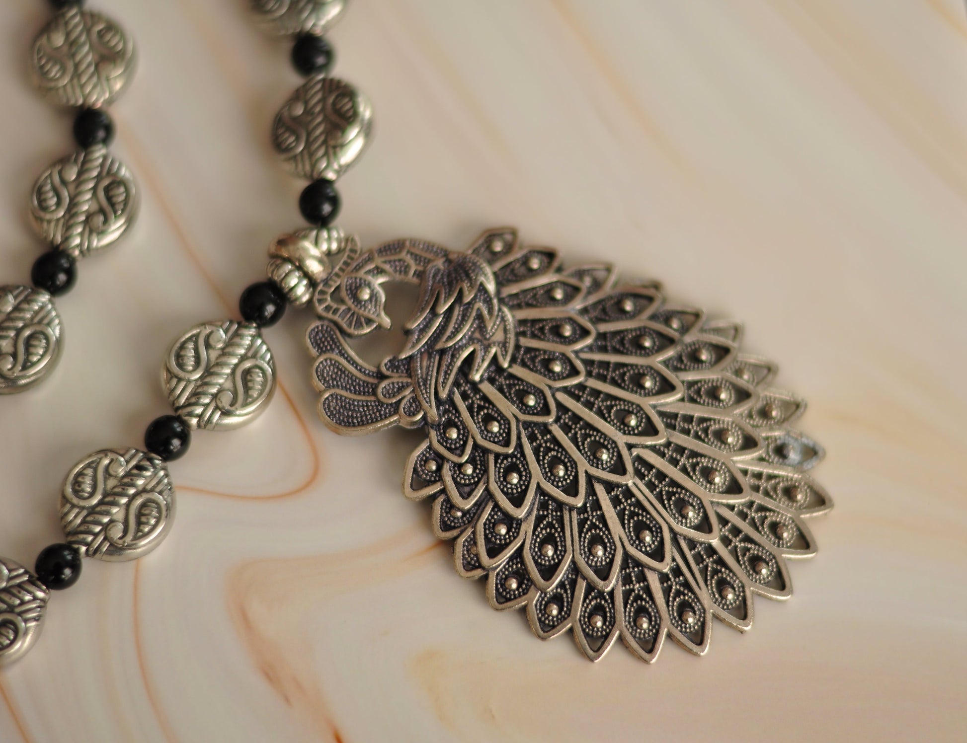 Silver peacock pendant necklace with intricate detailing and black bead accents, stylish bohemian jewelry.