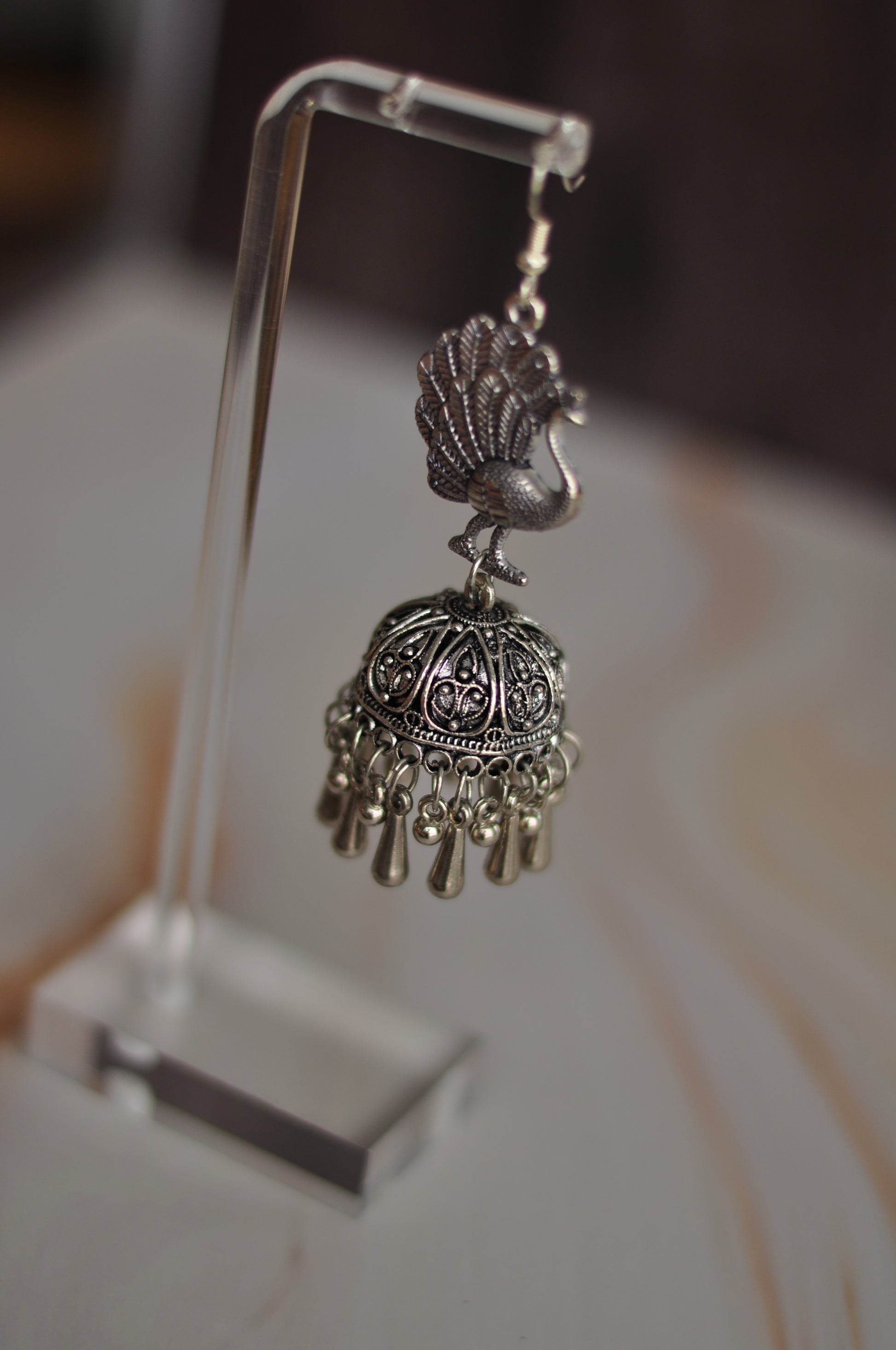 Silver peacock jhumka earrings with intricate detailing and dangling charms, perfect for traditional wear.