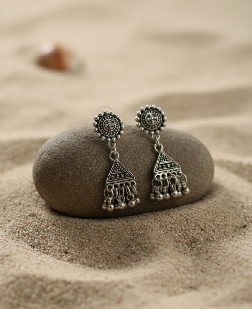 Silver bohemian earrings with intricate designs and dangling beads on a sandy background.