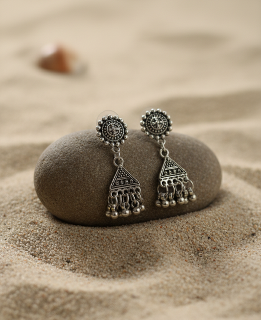 Silver bohemian earrings with intricate designs and dangling beads on a sandy background.