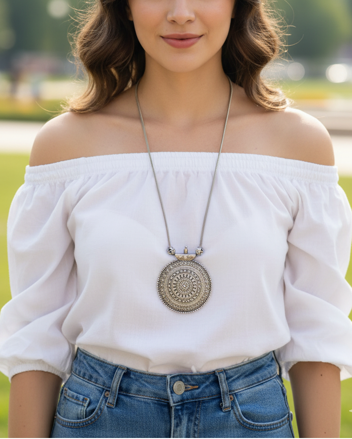 Silver pendant necklace featured on a woman in a white off-shoulder top, with intricate detailing.