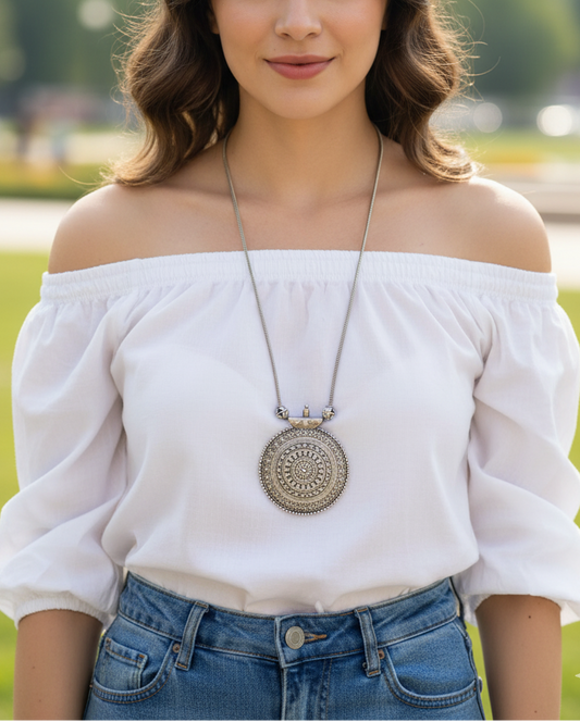Silver pendant necklace featured on a woman in a white off-shoulder top, with intricate detailing.