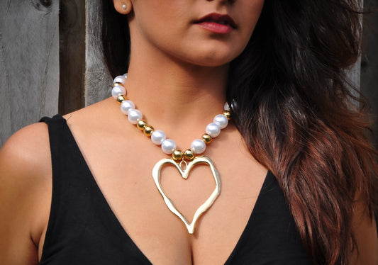 Stylish heart-shaped gold pendant necklace with white pearls and golden beads, perfect for elegant outfits.