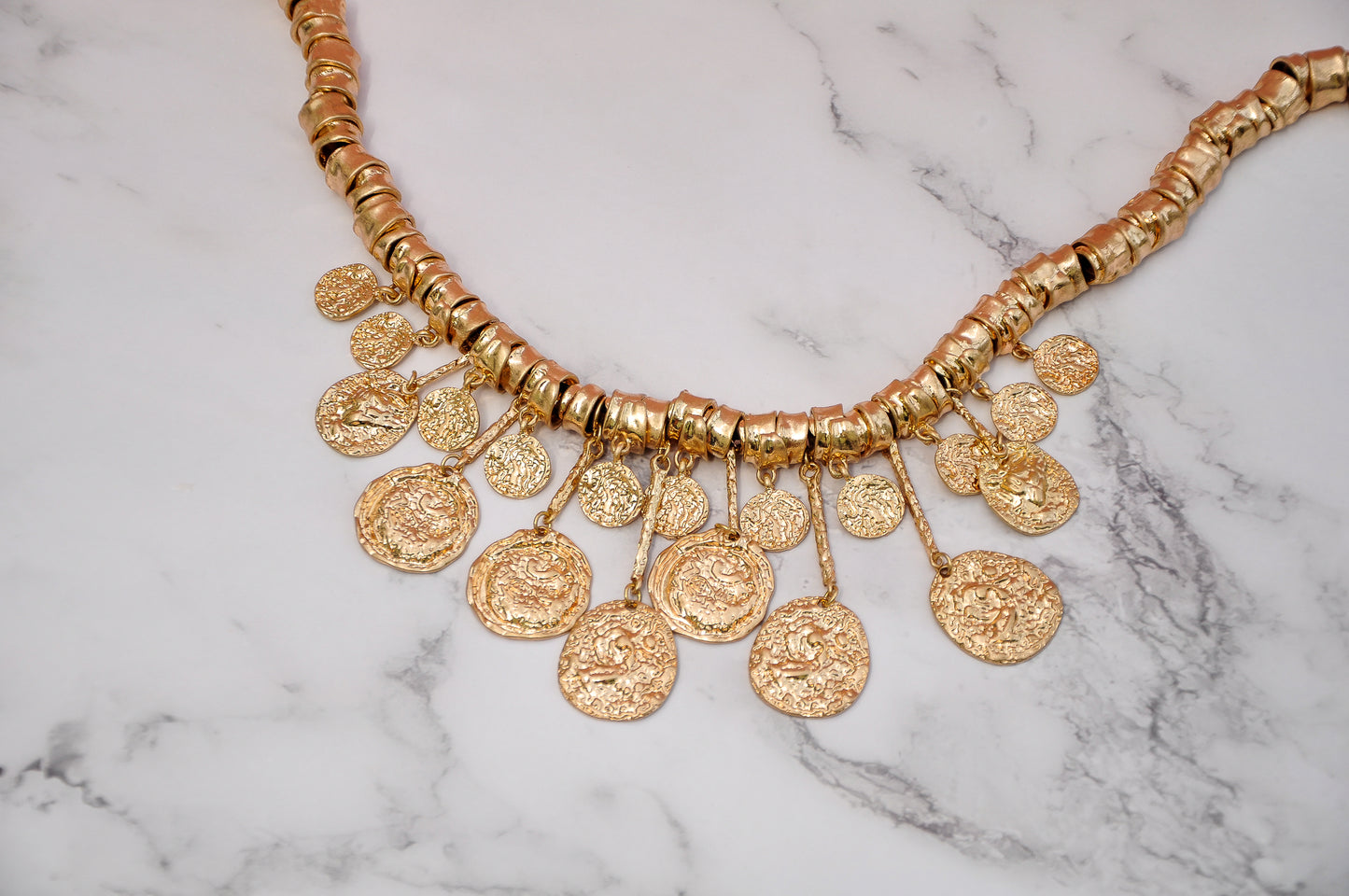 Elegant tribal themed statement necklace with hammered coins design against a white marble top