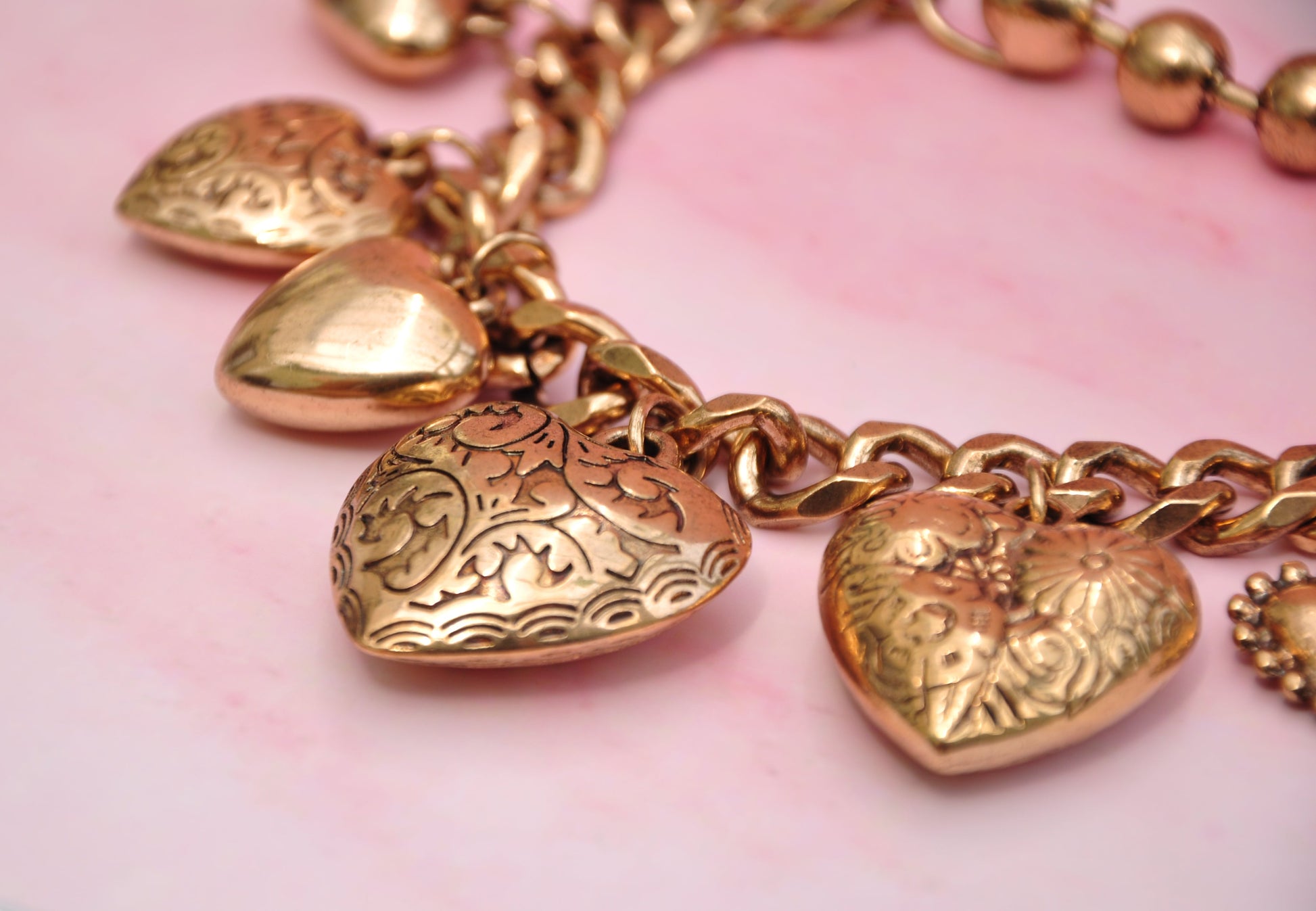 Rose gold heart charm bracelet with engraved designs and a chunky chain for a stylish look.