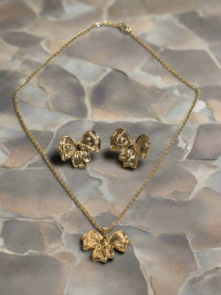 Gold necklace and earrings set featuring textured bow design on a stone background.