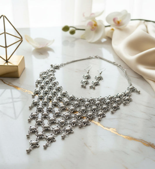 Silver statement necklace and earrings set with intricate design on marble surface.