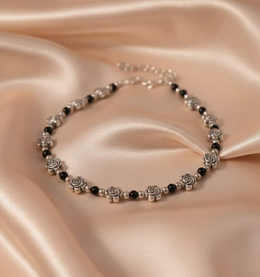 Elegant silver rose bracelet with black beads on a soft fabric background.