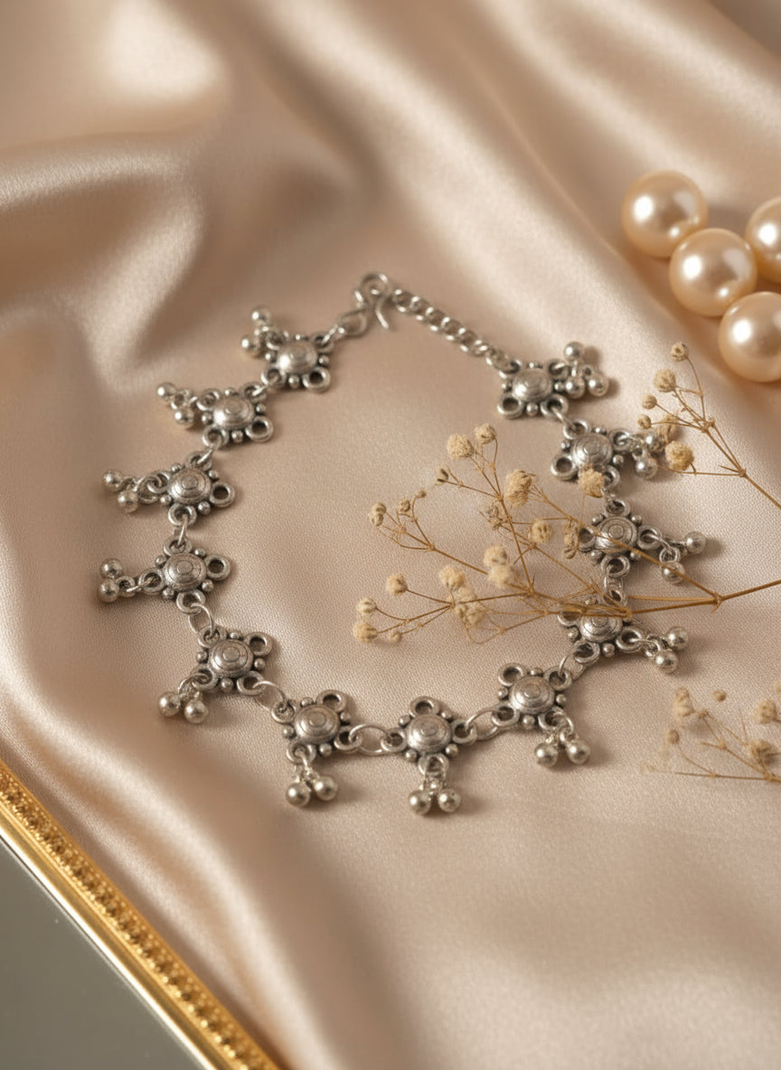 Elegant silver bracelet with intricate design and bead accents, set on satin fabric.