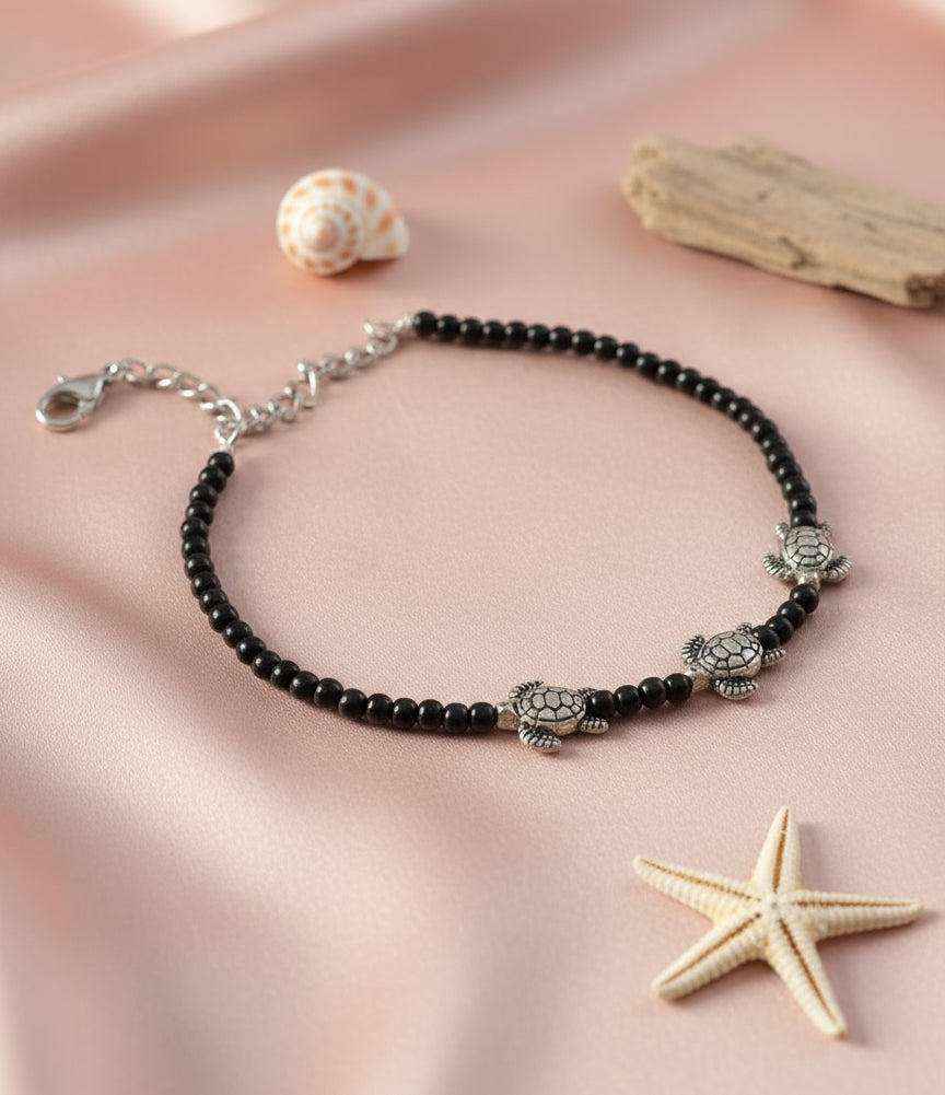 Black beaded bracelet with silver turtle charms, perfect for ocean lovers and beach enthusiasts.