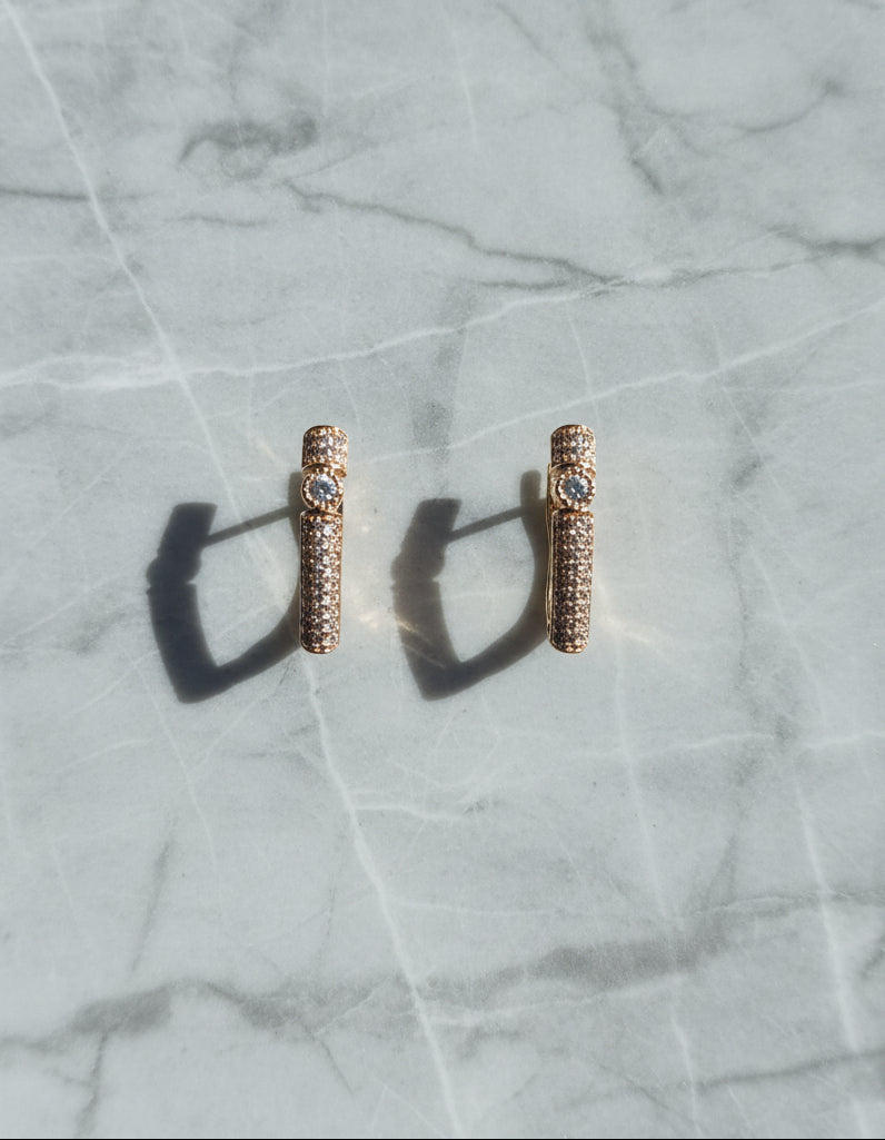 Rose gold stud earrings with crystal details on a marble background.