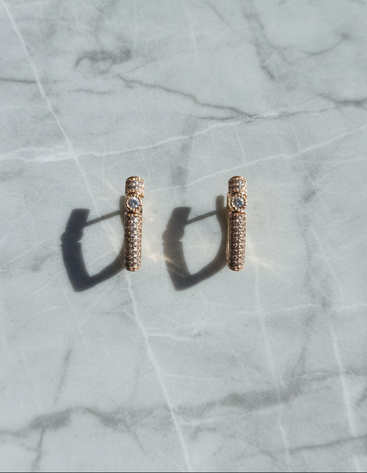 Rose gold stud earrings with crystal details on a marble background.