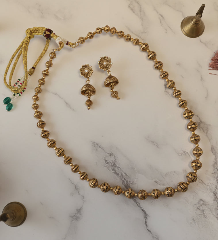 Elegant gold-plated necklace with matching earrings, featuring intricate designs and vibrant green accents.