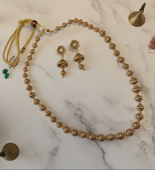 Elegant gold-plated necklace with matching earrings, featuring intricate designs and vibrant green accents.