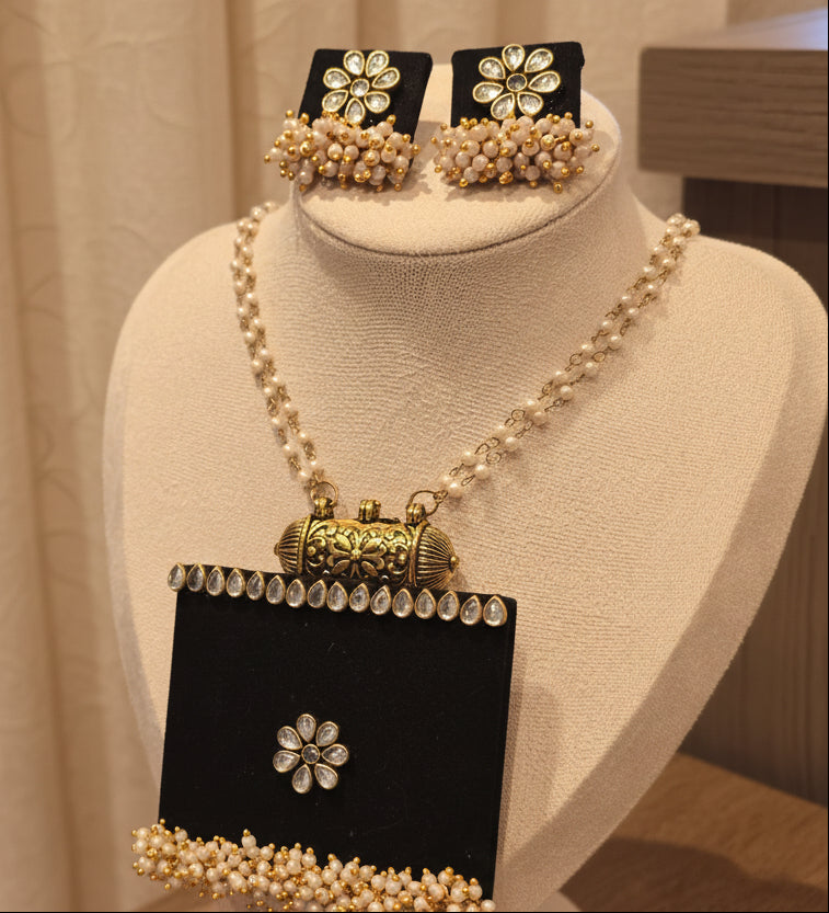 Elegant gold-tone jewelry set featuring a pearl necklace and matching stud earrings on display.