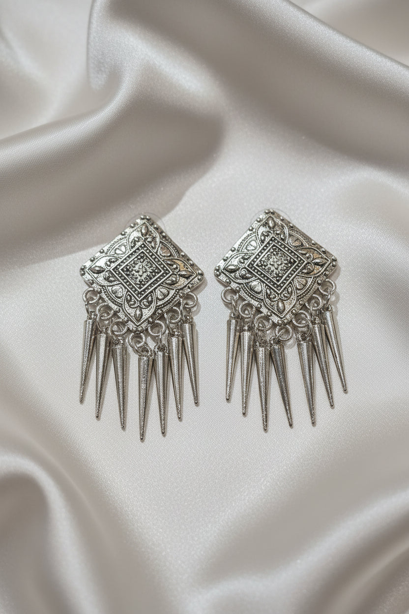 Silver statement earrings with ornate design and dangling spikes, perfect for formal occasions.