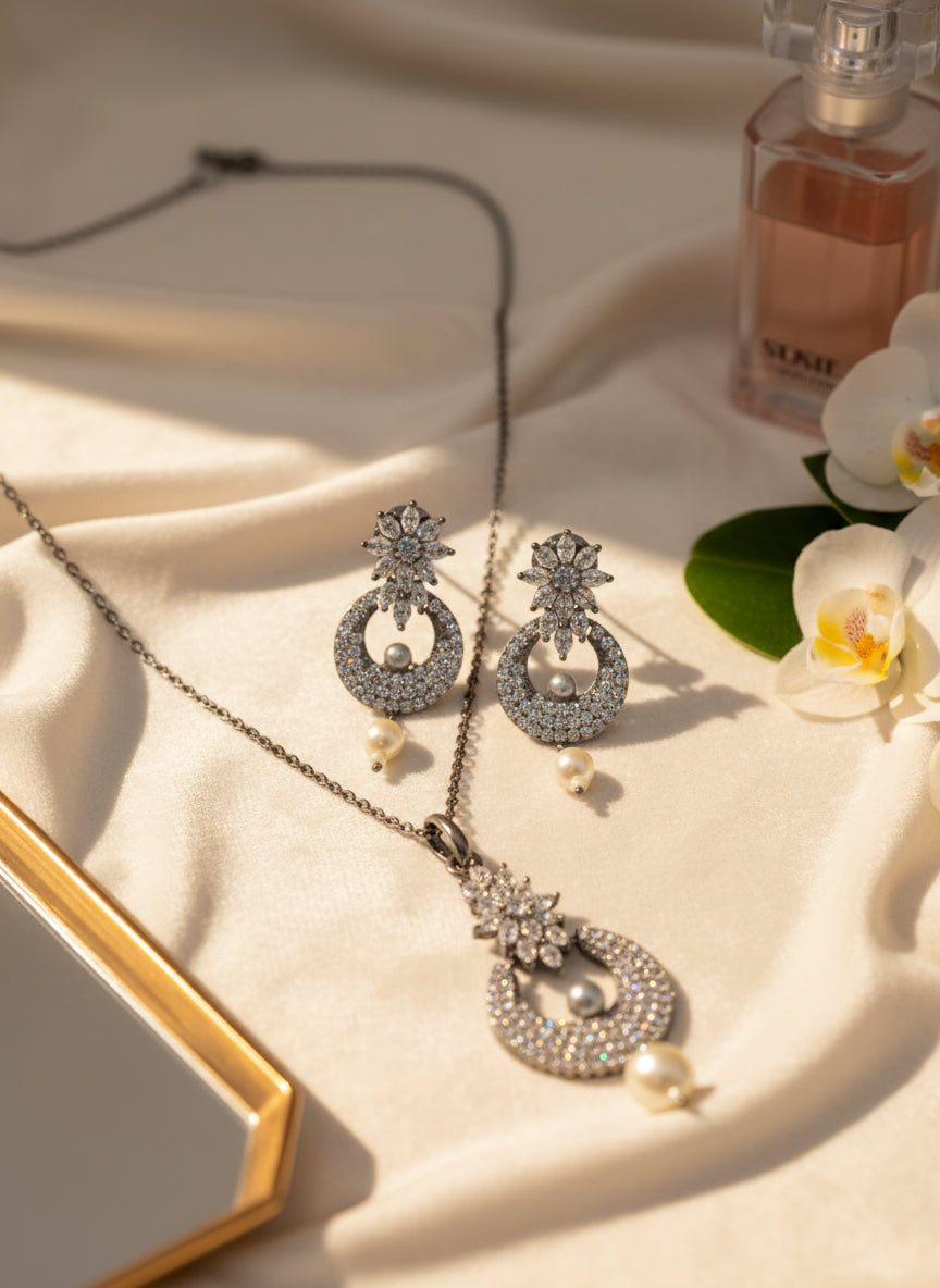 Elegant silver jewelry set featuring sparkly earrings and a pendant with pearls, displayed on soft fabric.