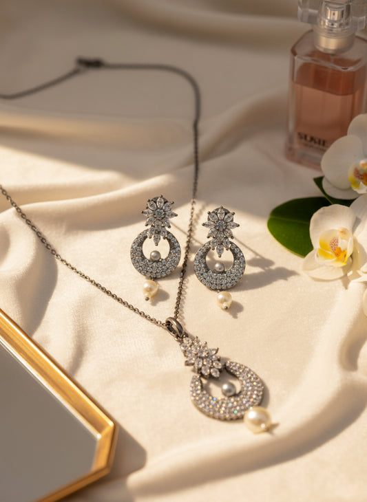 Elegant silver jewelry set featuring sparkly earrings and a pendant with pearls, displayed on soft fabric.