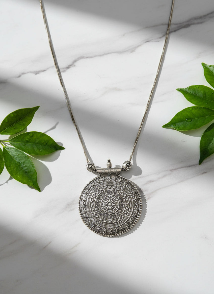 Silver pendant necklace with intricate circular design and snake chain, ideal for stylish outfits.