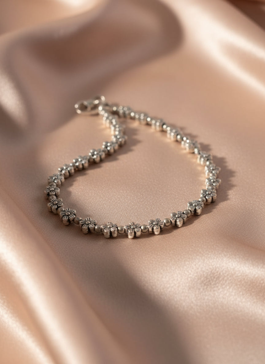 Silver flower charm bracelet on satin fabric, featuring delicate floral designs and a secure clasp.