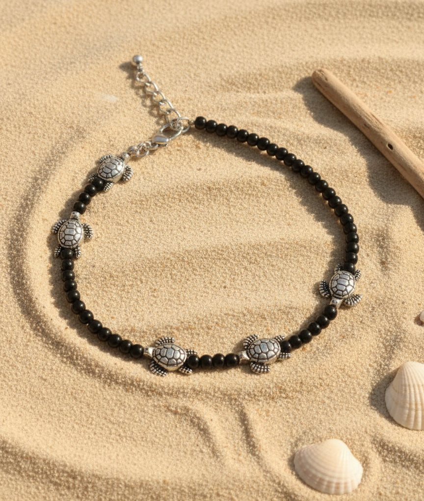 Black beaded anklet with silver turtle charms, perfect beach accessory for summer style.