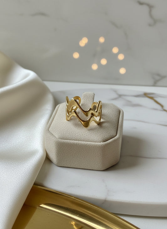 Gold wave ring on a beige display, featuring a stylish wavy design made of metal.