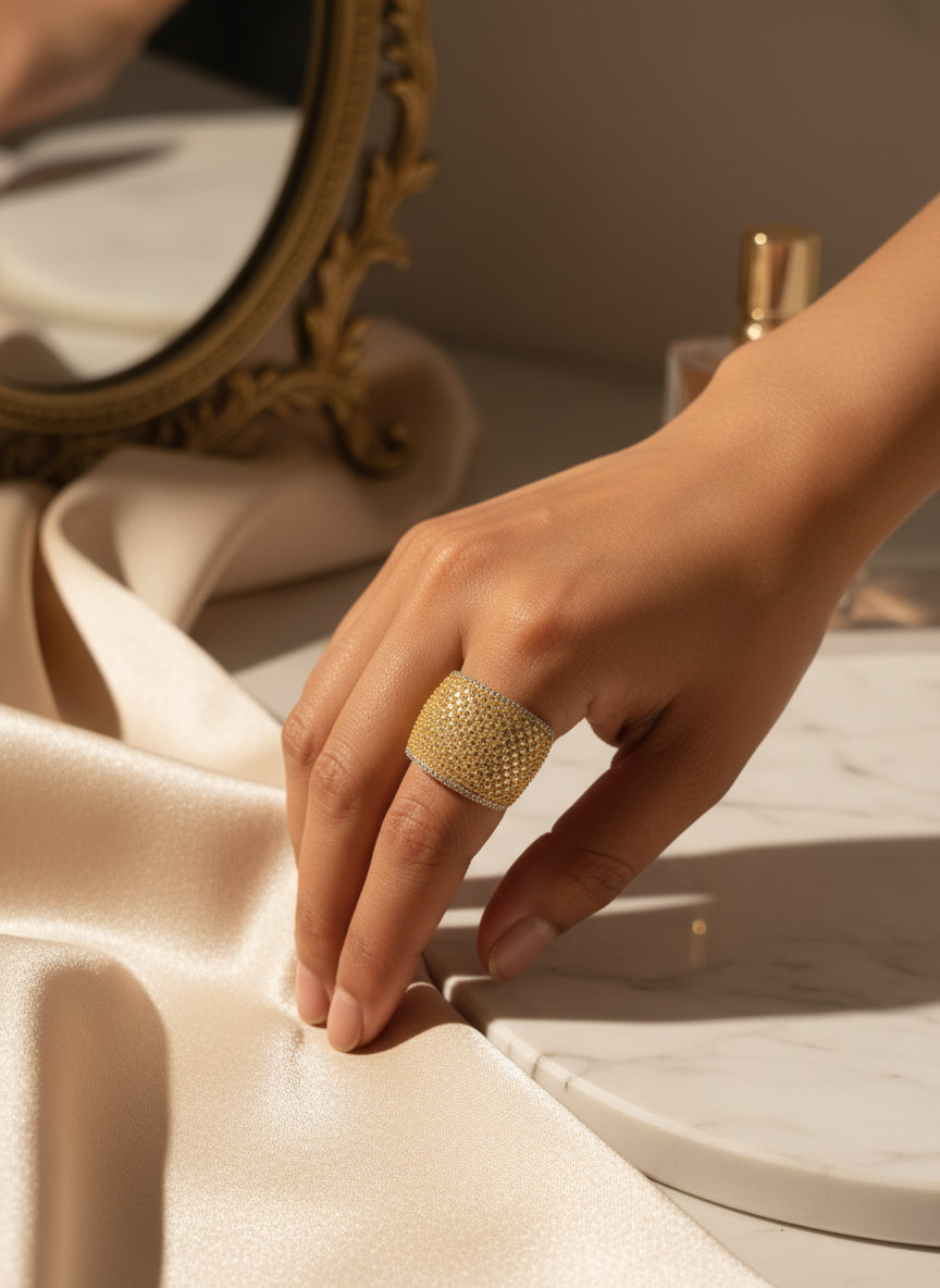 Elegant gold statement ring with sparkling crystals, highlighted on a soft satin surface.