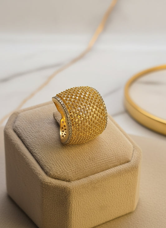 Elegant gold statement ring with shimmering pave stones on a soft display pedestal.