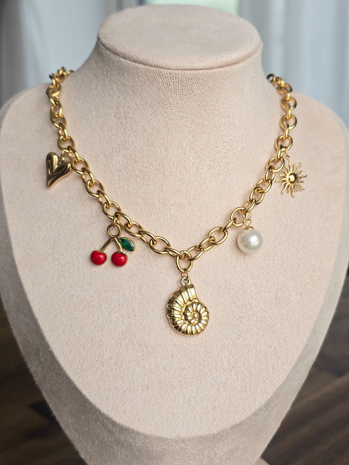 Stylish gold charm necklace featuring heart, cherry, sun, and seashell pendants on a chunky chain.