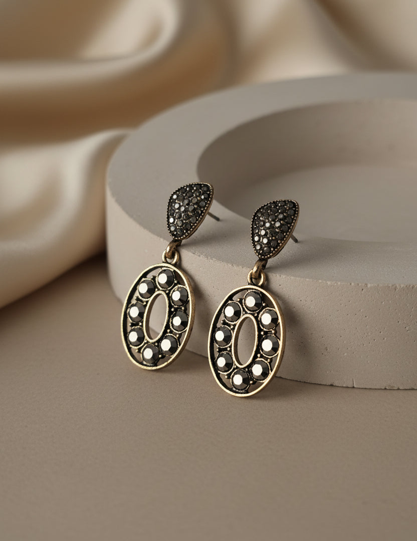 Gold-tone drop earrings with black and white stones, featuring an oval design and teardrop stud.