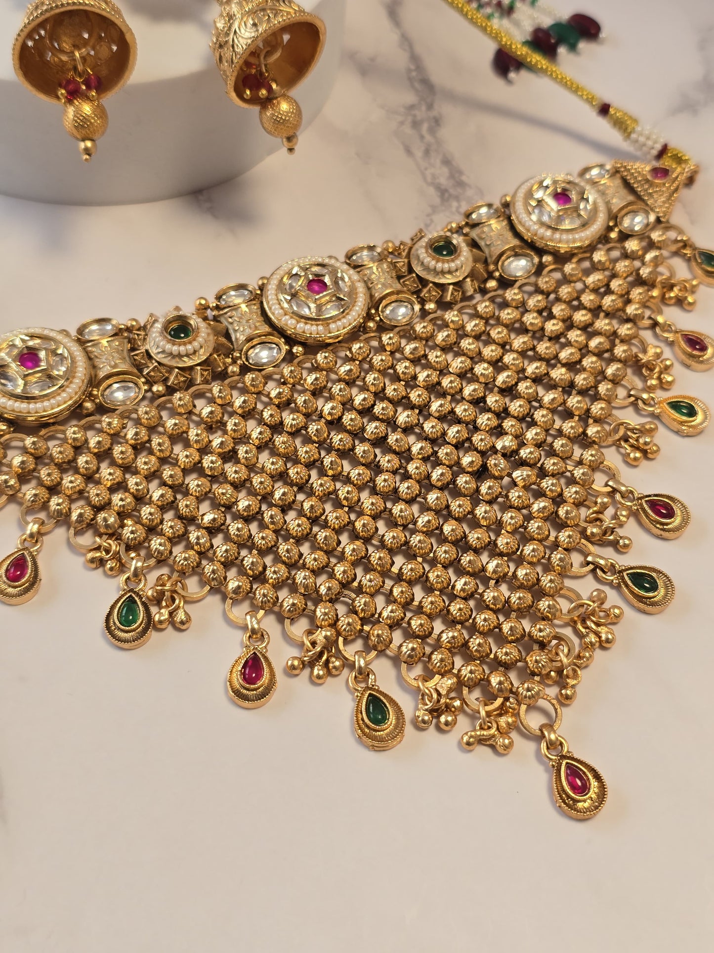 Traditional gold jewelry set with intricate design, featuring multi-colored gemstones and elegant dangling elements.