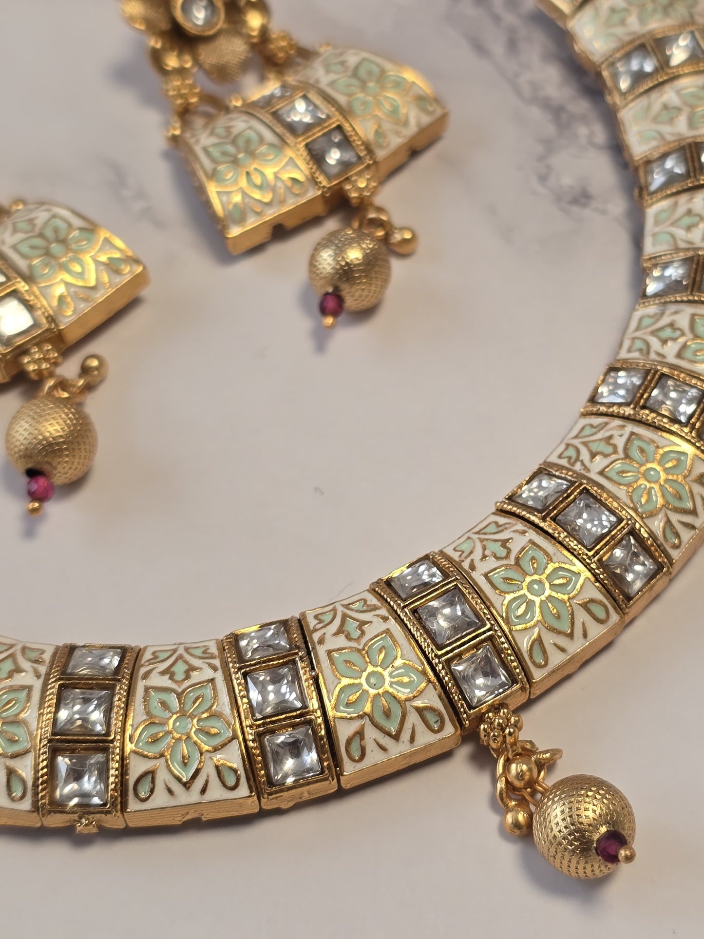 Traditional gold necklace set with intricate floral design, studded with crystals and colorful accents.