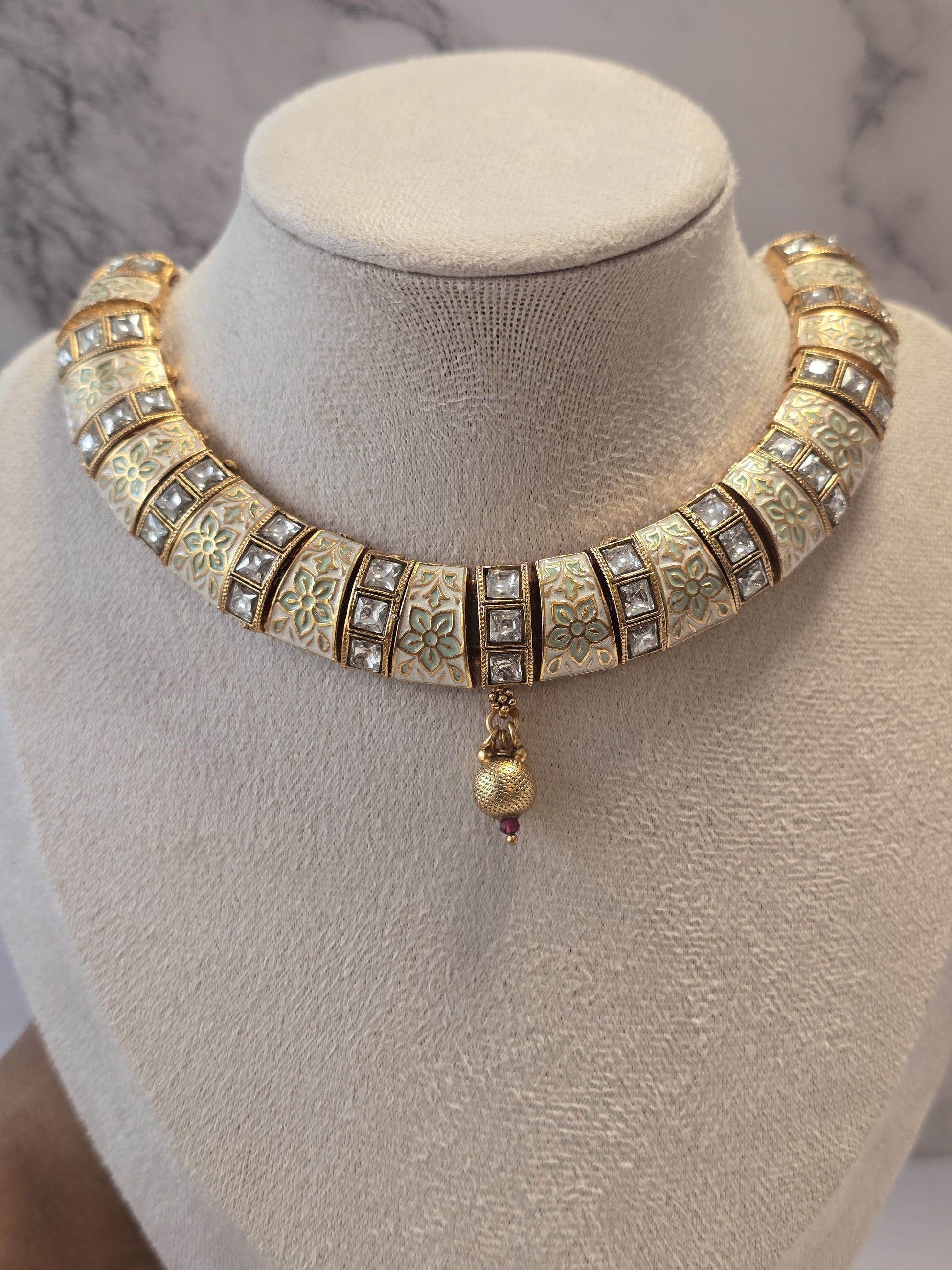 Traditional gold statement necklace with intricate enamel design and sparkling stones, featuring a decorative pendant.
